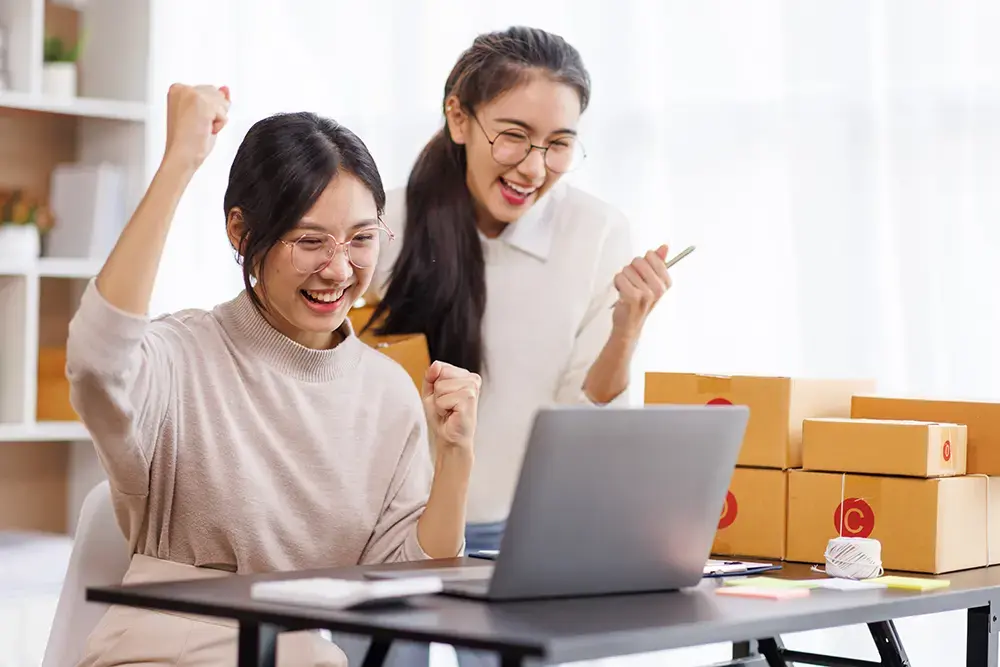 Shows two people looking at a laptop and cheering after picking the best inventory management tools for their business.