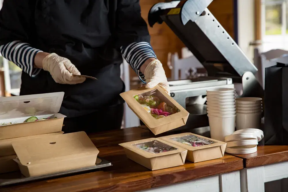 Shows a food business owner packing sides they may cross-sell to customers purchasing their main dishes.