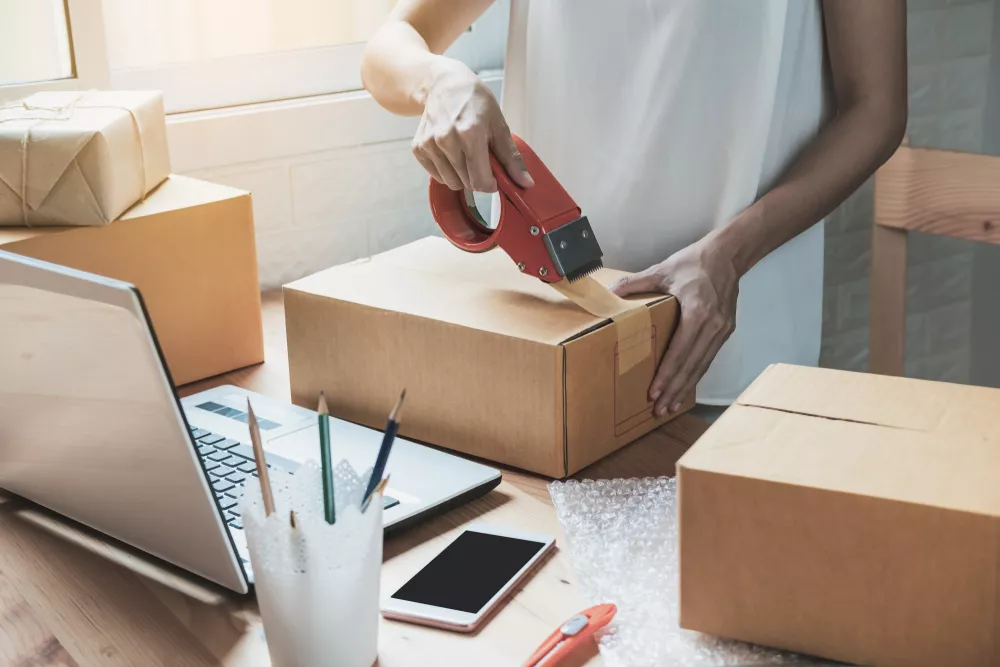 Shows a worker taping a package to ship to the buyer's doorstep for the customers' convenience.