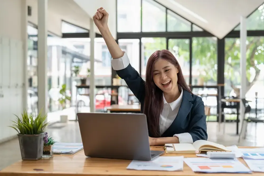 On a laptop, a business owner analyzes and celebrates the positive cash flow of their eCommerce business.