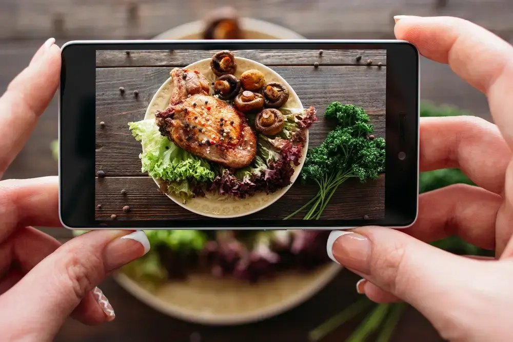 A person takes a photo of plated food to be used in online promotional materials.