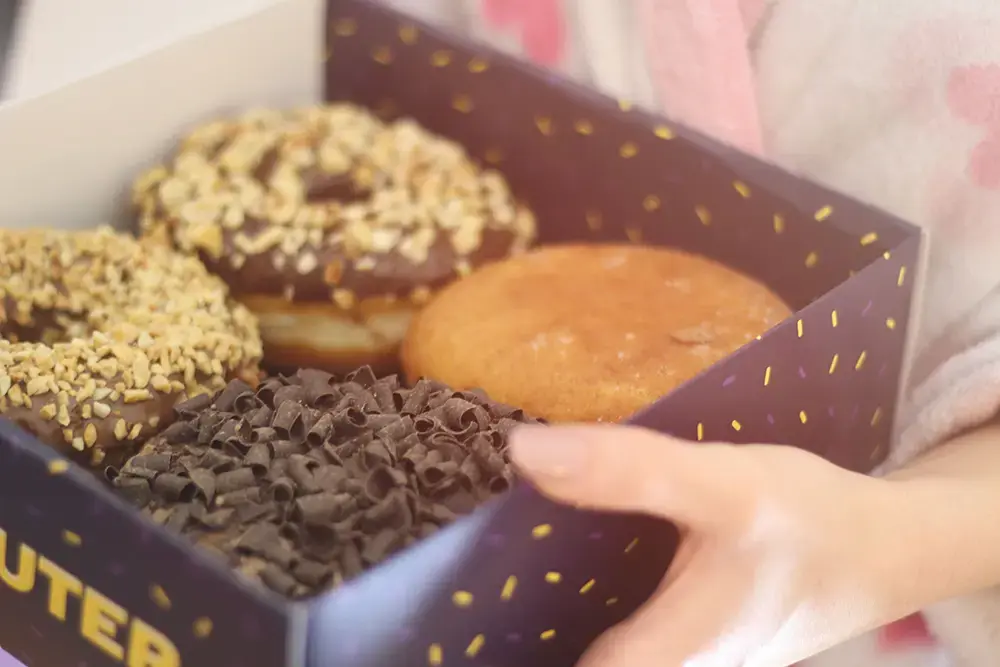 Shows a box of donuts in seasonal packaging, adding a special touch to encourage purchases.