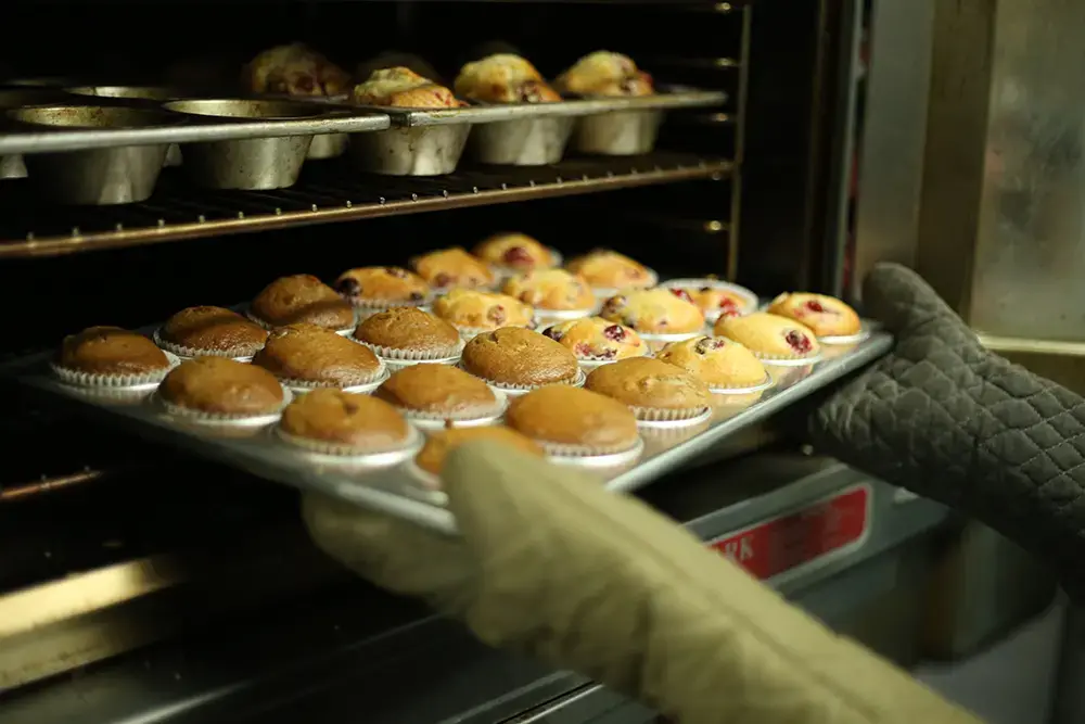 Someone managing the operations of their food business, pulling a fresh batch of muffins from the oven.