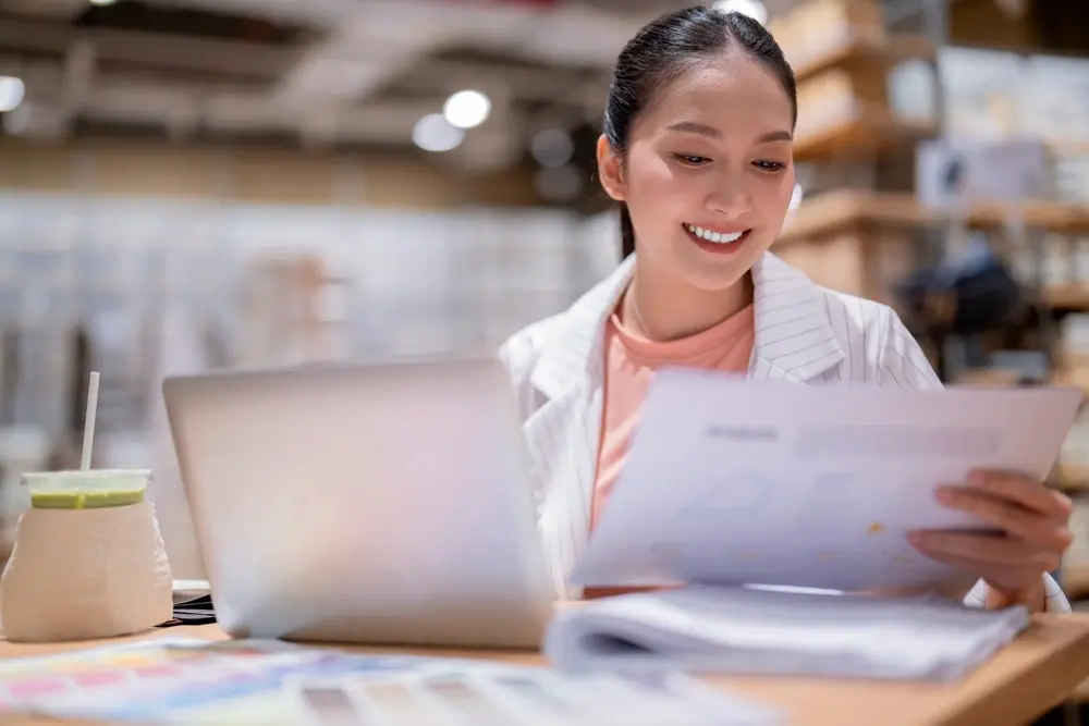 A woman smiles at warehouse reports, showing the results of seamless supply chain practices with RUSH.