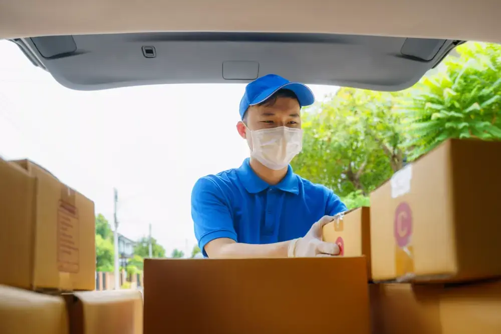 A delivery man places packages in the trunk of a car, showing the operations of a shipping company.