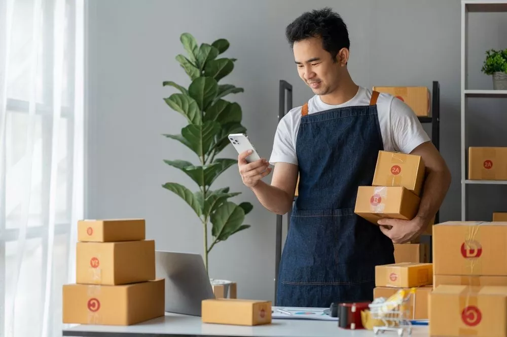 A business owner smiles at their phone, managing their eCommerce inventory easily with RUSH.