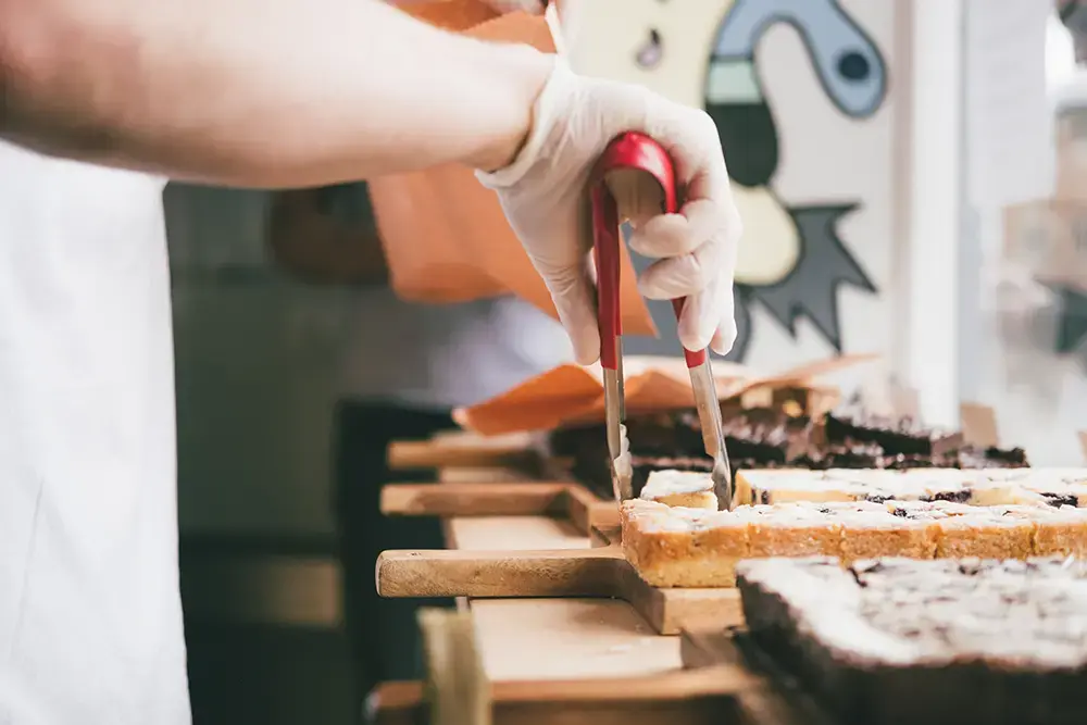 Shows a bakery worker selling brownies and placing them into takeout packaging.