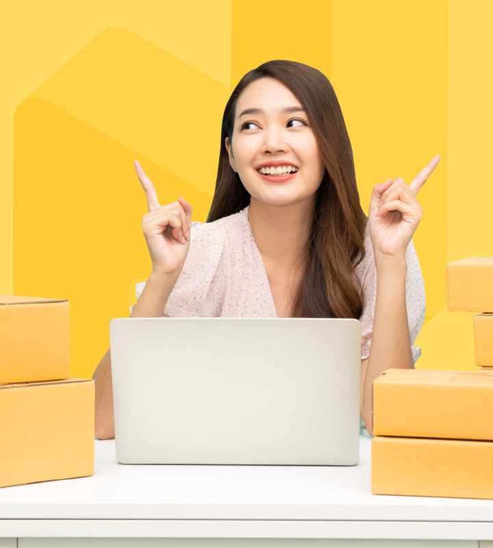 Is the main image for RUSH's eStore Program pricing and included features, but shows a woman behind a laptop and boxes of orders, looking happy as she manages her online store.